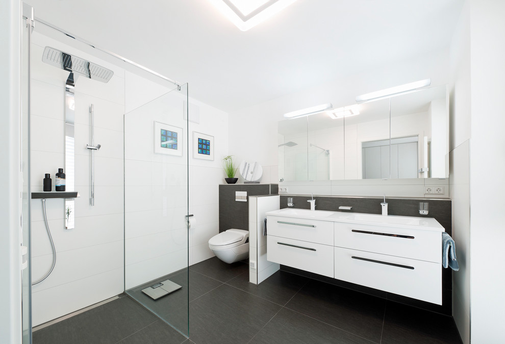 Medium sized contemporary bathroom in Stuttgart with flat-panel cabinets, white cabinets, a built-in shower, a wall mounted toilet, grey tiles, stone slabs, white walls, a trough sink, slate flooring and an open shower.
