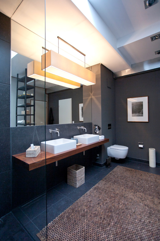 Идея дизайна: ванная комната в современном стиле с черной плиткой, столешницей из дерева, инсталляцией, серыми стенами, настольной раковиной, отдельно стоящей ванной, открытым душем, коричневой столешницей и зеркалом с подсветкой