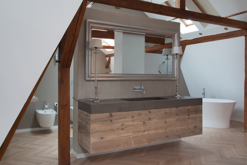 Ejemplo de cuarto de baño rústico de tamaño medio con bañera exenta, ducha a ras de suelo, sanitario de pared, paredes grises, suelo de madera en tonos medios y lavabo integrado