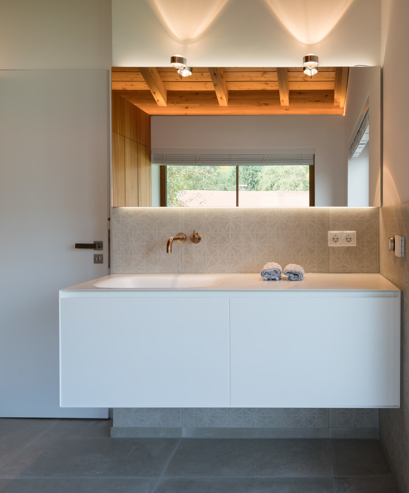 Modelo de cuarto de baño principal actual de tamaño medio con bañera exenta, paredes blancas, lavabo integrado, encimera de acrílico, suelo gris y encimeras blancas