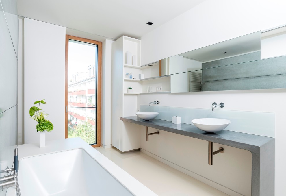 This is an example of a medium sized contemporary ensuite bathroom in Hamburg with flat-panel cabinets, white cabinets, a submerged bath, white walls, vinyl flooring, a vessel sink and concrete worktops.
