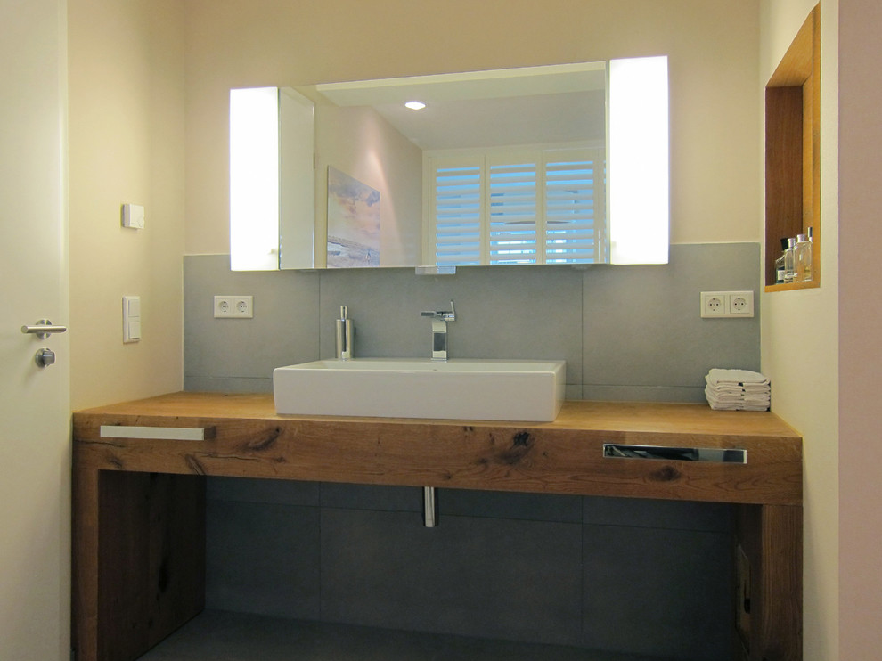 Modelo de cuarto de baño contemporáneo con lavabo sobreencimera, encimera de madera, bañera encastrada, ducha a ras de suelo, sanitario de pared, baldosas y/o azulejos grises, baldosas y/o azulejos de cerámica y suelo de baldosas de cerámica