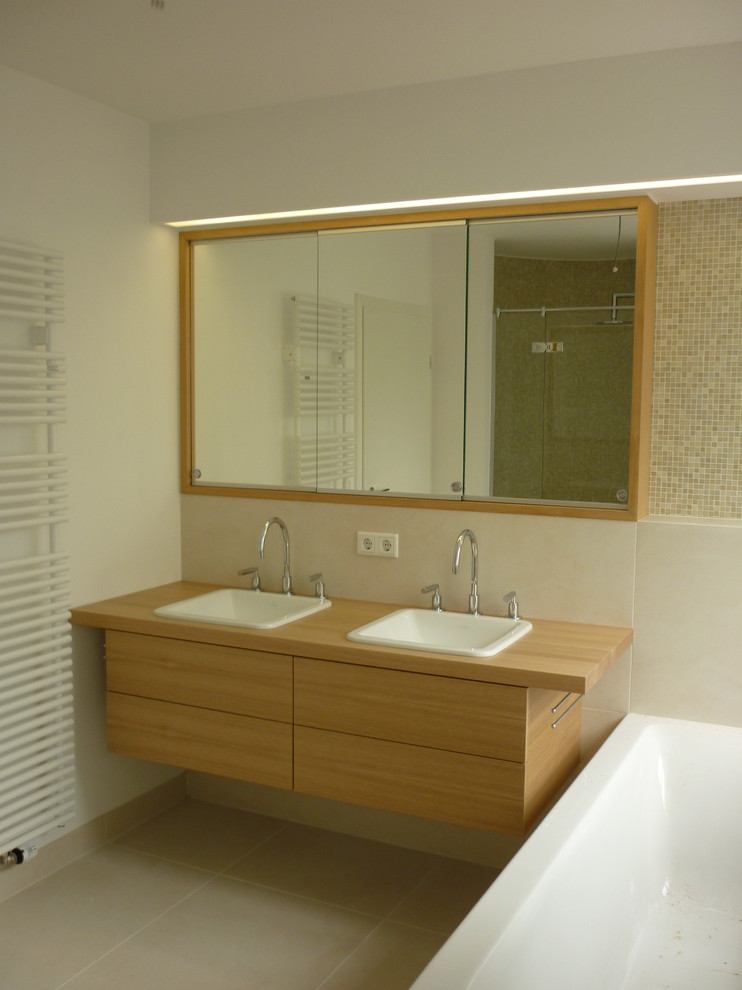 Cette photo montre une petite salle de bain principale tendance en bois brun avec un placard à porte plane, un carrelage beige, un mur blanc, un lavabo posé, un plan de toilette en bois, une baignoire posée, WC suspendus, des carreaux de porcelaine, carreaux de ciment au sol et un sol beige.