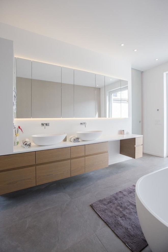 Inspiration for a large contemporary bathroom in Berlin with flat-panel cabinets, medium wood cabinets, a freestanding bath, grey tiles, stone tiles, white walls, slate flooring, a vessel sink and solid surface worktops.