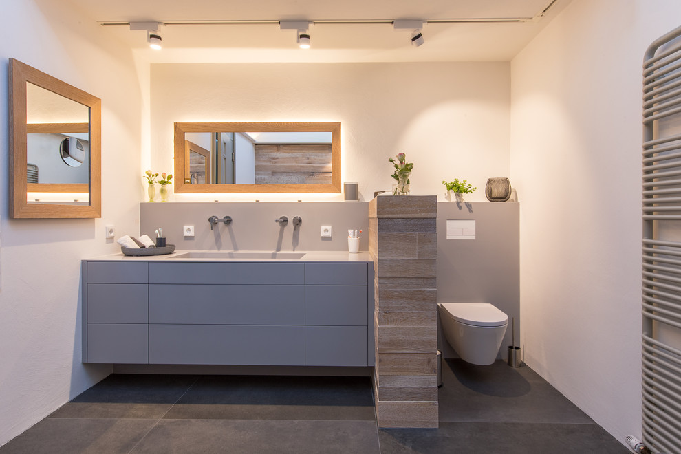 Стильный дизайн: ванная комната среднего размера: освещение в современном стиле с плоскими фасадами, серыми фасадами, инсталляцией, бежевой плиткой, коричневой плиткой, белыми стенами, полом из цементной плитки, монолитной раковиной и коричневым полом - последний тренд