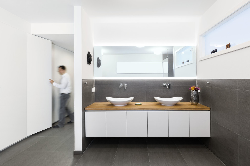 Cette photo montre un sauna tendance de taille moyenne avec un placard à porte plane, des portes de placard blanches, une baignoire indépendante, un carrelage gris, des carreaux de céramique, une vasque et un plan de toilette en bois.