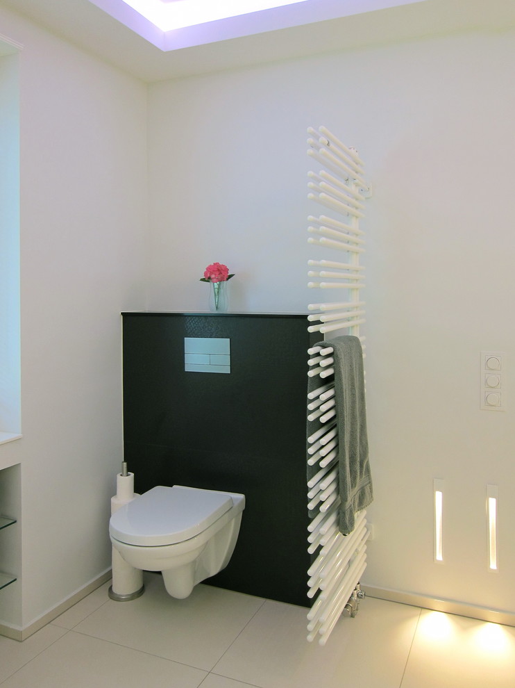 Photo of a medium sized contemporary ensuite bathroom in Cologne with flat-panel cabinets, white cabinets, a built-in bath, a built-in shower, a wall mounted toilet, black tiles, ceramic tiles, white walls, ceramic flooring, a built-in sink and solid surface worktops.