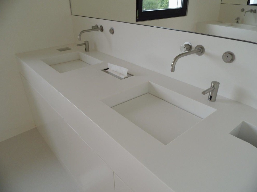 Inspiration for a modern bathroom in Dortmund with white cabinets, a trough sink and solid surface worktops.