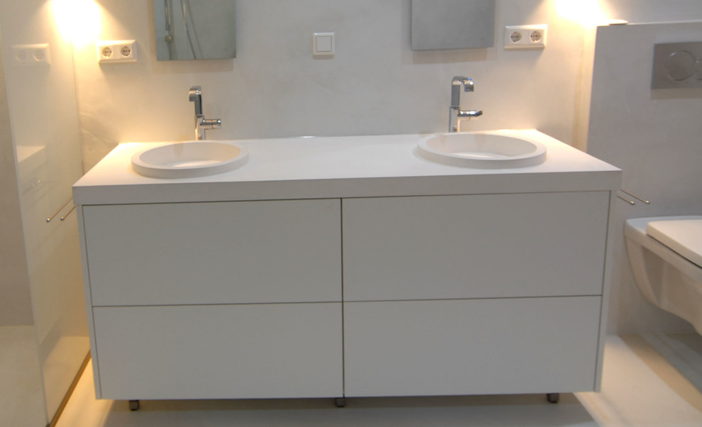 Modelo de cuarto de baño actual con puertas de armario blancas, ducha a ras de suelo, sanitario de pared, paredes blancas y lavabo de seno grande