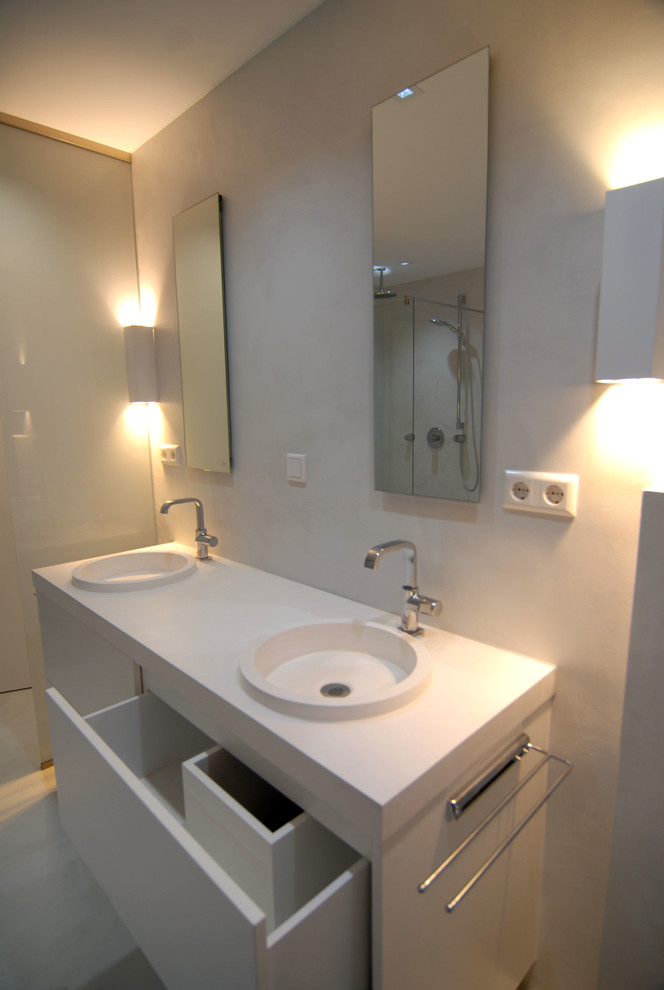 На фото: ванная комната в современном стиле с белыми фасадами, душем без бортиков, белыми стенами и раковиной с несколькими смесителями