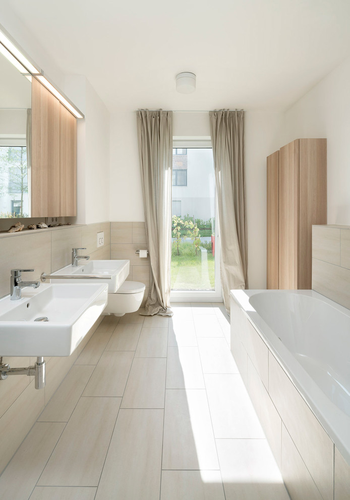 На фото: ванная комната среднего размера в современном стиле с накладной ванной, инсталляцией, бежевой плиткой, белыми стенами и подвесной раковиной с