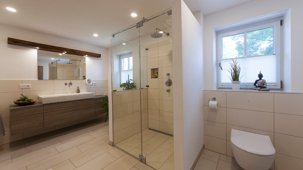 Example of a large 3/4 beige tile cement tile floor and beige floor walk-in shower design in Munich with flat-panel cabinets, medium tone wood cabinets, a wall-mount toilet, white walls, a vessel sink, wood countertops and a hinged shower door