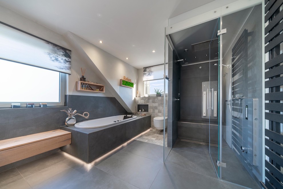 Example of a large trendy gray tile and stone tile ceramic tile and gray floor bathroom design in Stuttgart with light wood cabinets, a hot tub, a two-piece toilet, white walls, a vessel sink, a hinged shower door and brown countertops