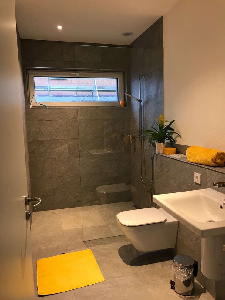 Inredning av ett modernt mellanstort badrum, med grå väggar, ett konsol handfat, grått golv, en kantlös dusch, en toalettstol med separat cisternkåpa och med dusch som är öppen