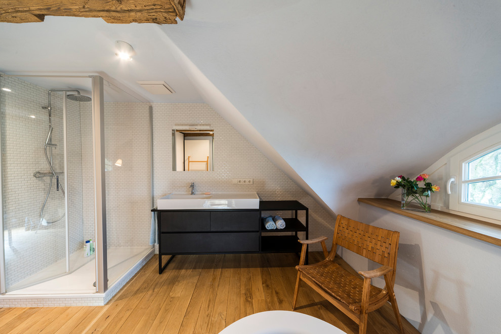 Idéer för mellanstora skandinaviska badrum med dusch, med släta luckor, svarta skåp, en hörndusch, vit kakel, vita väggar, mellanmörkt trägolv, ett fristående handfat, brunt golv och dusch med gångjärnsdörr