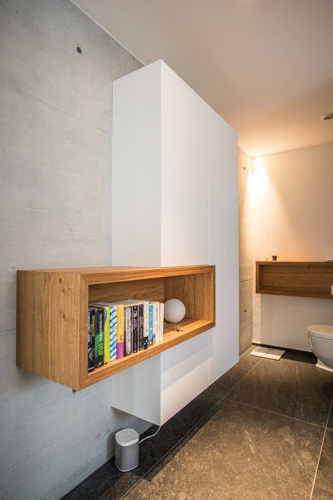 Foto de cuarto de baño actual de tamaño medio con armarios con paneles lisos, puertas de armario blancas, sanitario de pared, paredes blancas y suelo negro
