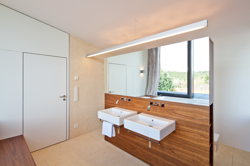 На фото: большая ванная комната в современном стиле с открытыми фасадами, фасадами цвета дерева среднего тона, накладной ванной, бежевой плиткой, каменной плиткой, белыми стенами, полом из известняка и подвесной раковиной с