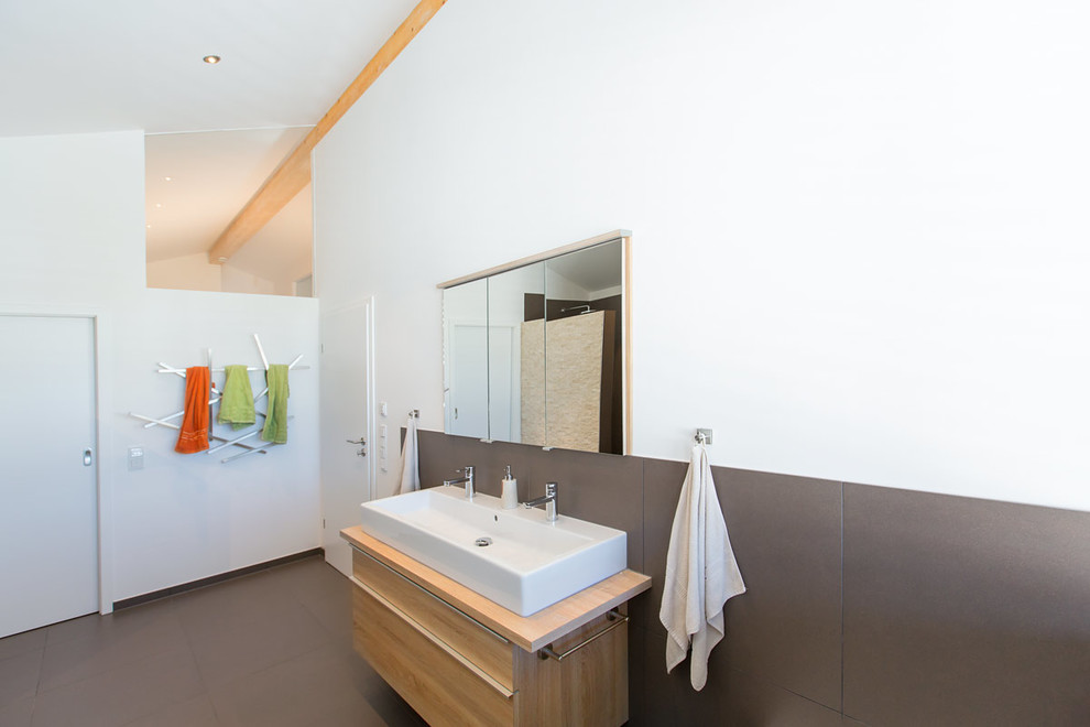 Foto di una stanza da bagno contemporanea di medie dimensioni con ante lisce, ante in legno chiaro, piastrelle grigie, piastrelle in pietra, pareti bianche, lavabo a bacinella e top in legno