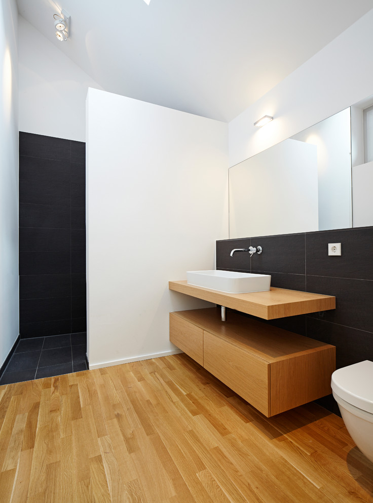 Свежая идея для дизайна: ванная комната среднего размера в современном стиле с плоскими фасадами, фасадами цвета дерева среднего тона, столешницей из дерева, душем в нише, черной плиткой, белыми стенами и душевой кабиной - отличное фото интерьера