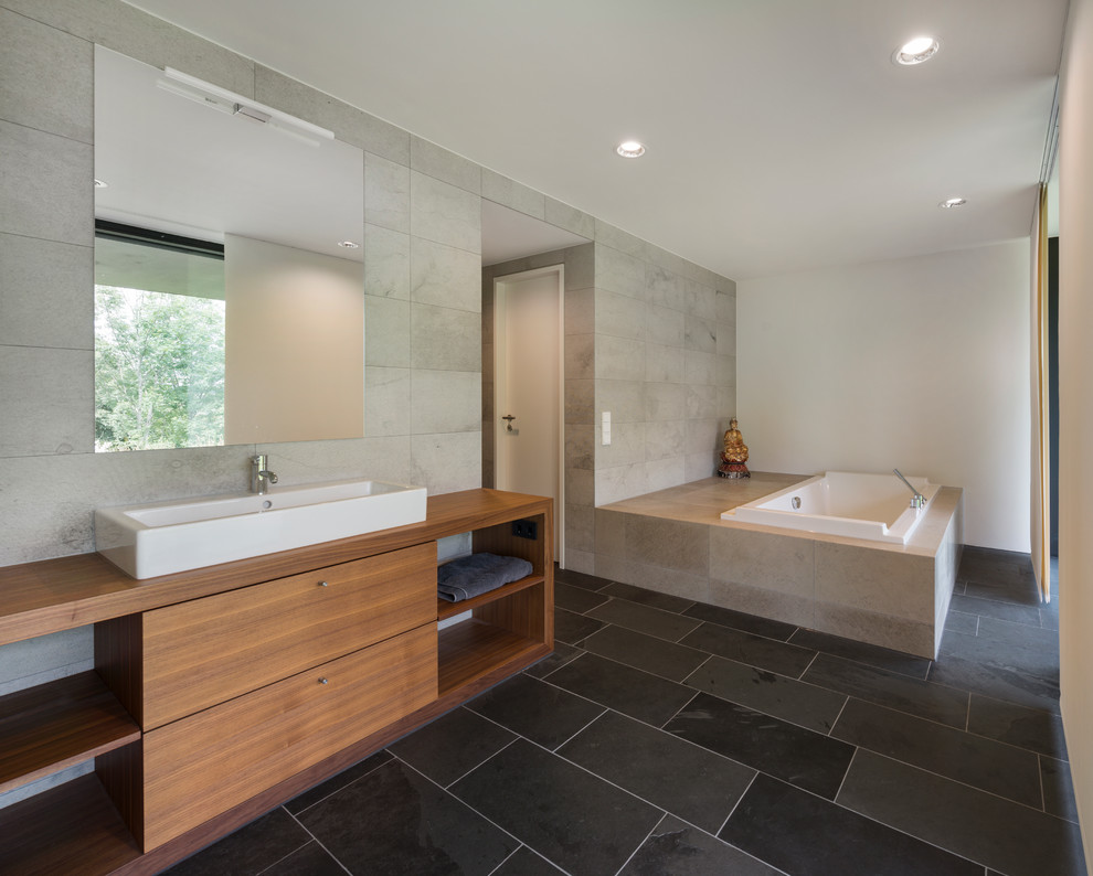 Drop-in bathtub - large contemporary gray tile slate floor drop-in bathtub idea in Other with a vessel sink, flat-panel cabinets, medium tone wood cabinets, wood countertops and white walls