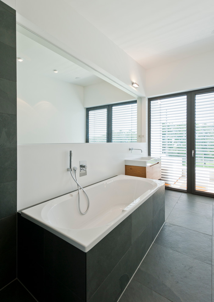 Exempel på ett stort modernt en-suite badrum, med släta luckor, skåp i ljust trä, ett platsbyggt badkar, en kantlös dusch, en vägghängd toalettstol, svart kakel, stenhäll, vita väggar, skiffergolv och ett väggmonterat handfat