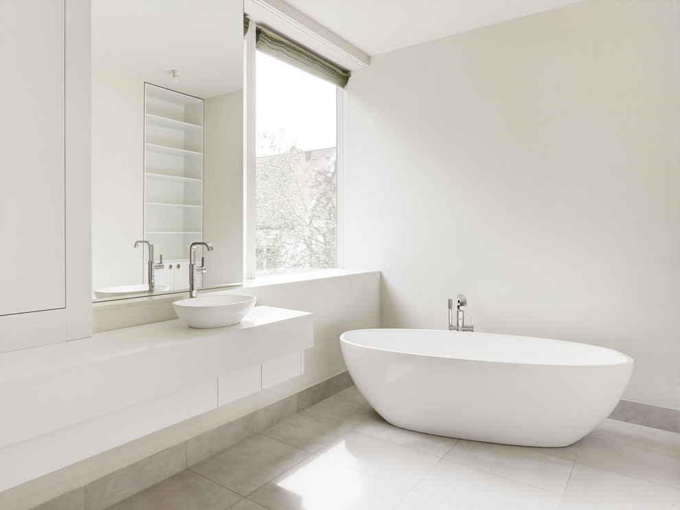 Idéer för mellanstora funkis en-suite badrum, med släta luckor, vita skåp, bänkskiva i akrylsten, beige kakel, keramikplattor, ett fristående badkar, vita väggar och ett fristående handfat
