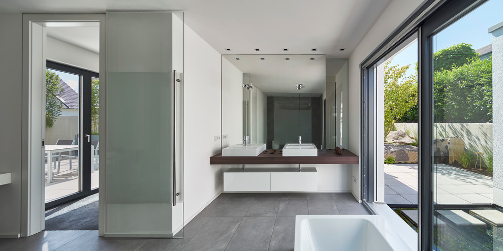 Foto de cuarto de baño minimalista grande con lavabo sobreencimera, armarios con paneles lisos, puertas de armario blancas, encimera de madera, baldosas y/o azulejos grises, baldosas y/o azulejos de piedra y paredes blancas