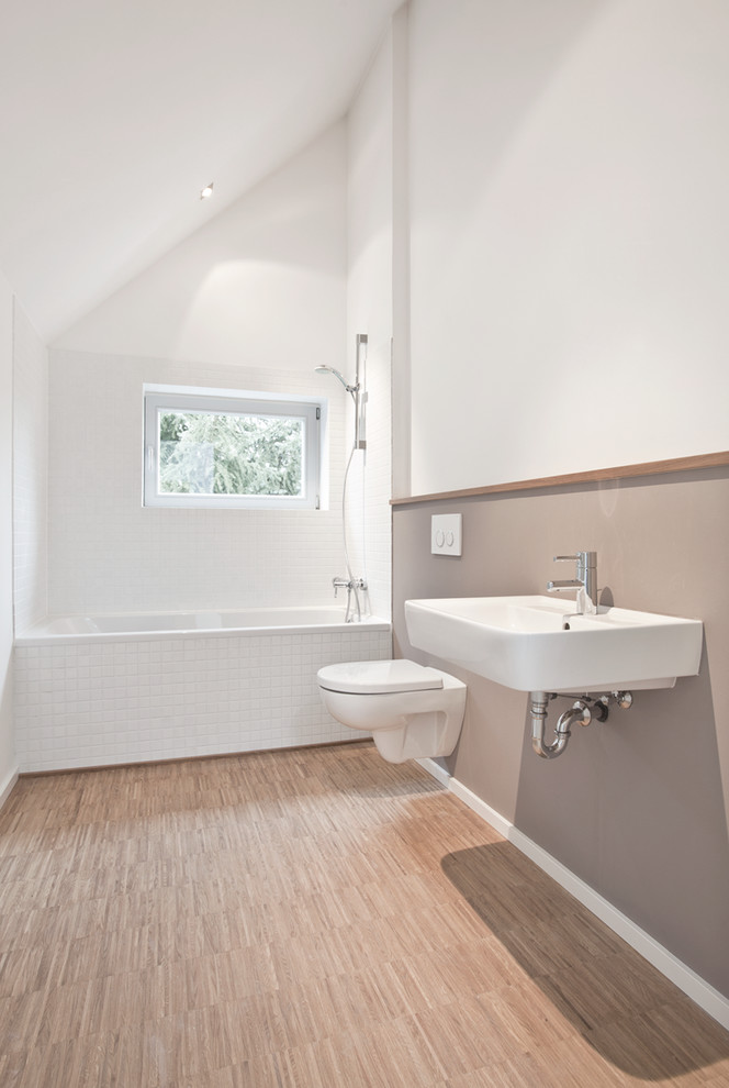 На фото: маленькая ванная комната в современном стиле с подвесной раковиной, ванной в нише, душем над ванной, белой плиткой, белыми стенами, инсталляцией, плиткой кабанчик и паркетным полом среднего тона для на участке и в саду с