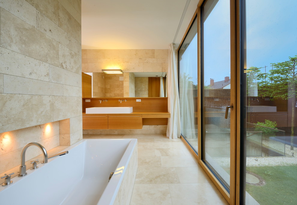 Cette photo montre une salle de bain tendance en bois brun avec un placard à porte plane, une baignoire posée et un carrelage beige.