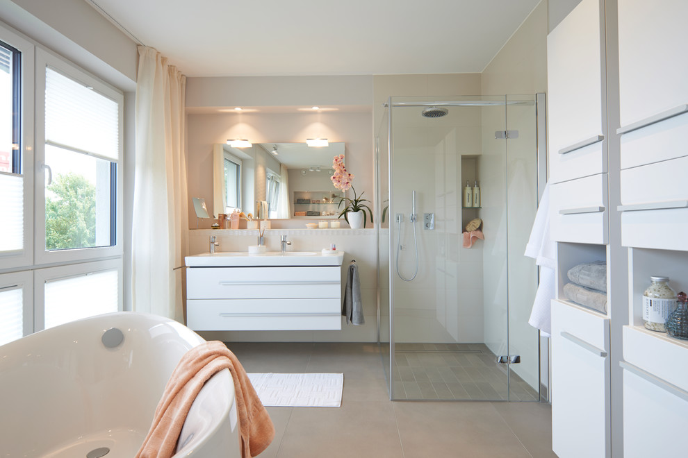 Idée de décoration pour une grande salle de bain design avec un placard à porte plane, des portes de placard blanches, une douche d'angle, un carrelage beige, un mur blanc, une baignoire indépendante et un lavabo intégré.