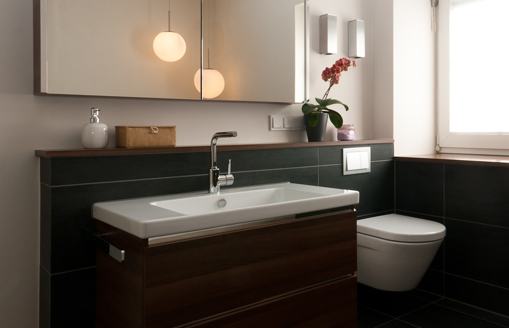 This is an example of a large contemporary ensuite bathroom in Frankfurt with flat-panel cabinets, dark wood cabinets, a built-in bath, a built-in shower, a two-piece toilet, black tiles, ceramic tiles, black walls, concrete flooring, a trough sink, black floors and an open shower.