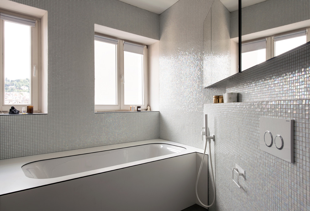 Photo of a small modern bathroom in Milan with glass-front cabinets, a submerged bath, a wall mounted toilet, green tiles, mosaic tiles, green walls, mosaic tile flooring and a console sink.