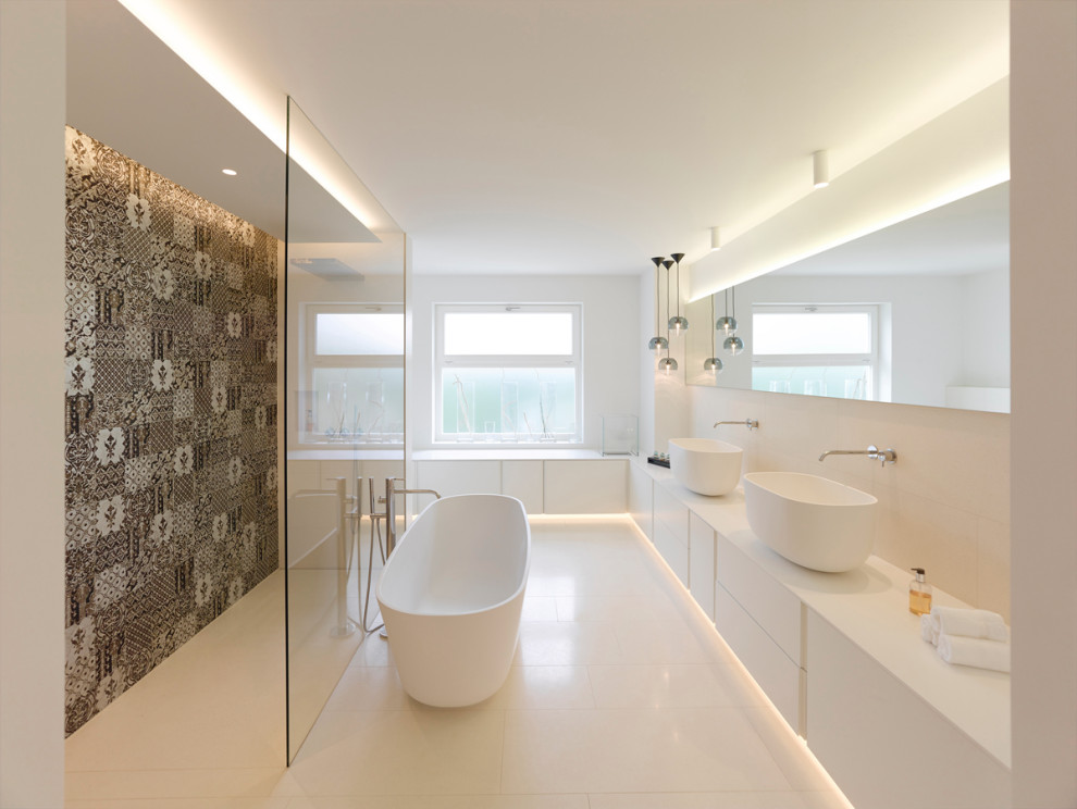 Large modern ensuite bathroom in Stuttgart with a freestanding bath, a built-in shower, ceramic flooring, solid surface worktops, an open shower, flat-panel cabinets, white cabinets, multi-coloured tiles, white walls, a vessel sink, white floors and white worktops.