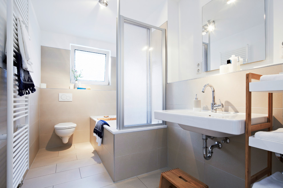 Idéer för att renovera ett litet funkis badrum med dusch, med ett platsbyggt badkar, en dusch/badkar-kombination, en vägghängd toalettstol, beige kakel, cementkakel, vita väggar, cementgolv, ett väggmonterat handfat, beiget golv och dusch med gångjärnsdörr