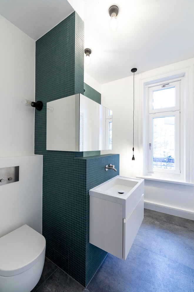 This is an example of a small contemporary shower room bathroom in Hamburg with flat-panel cabinets, white cabinets, a built-in bath, a shower/bath combination, a wall mounted toilet, green tiles, mosaic tiles, white walls, a wall-mounted sink, solid surface worktops, grey floors, an open shower and white worktops.