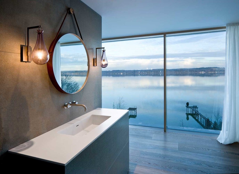 Свежая идея для дизайна: главная ванная комната среднего размера в современном стиле с плоскими фасадами, серыми фасадами, серыми стенами, деревянным полом, монолитной раковиной и столешницей из искусственного камня - отличное фото интерьера