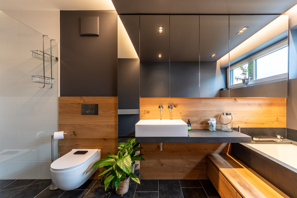 Exemple d'une salle d'eau tendance de taille moyenne avec WC suspendus, un carrelage marron, des carreaux de porcelaine, un mur noir, un sol en carrelage de porcelaine, une vasque, un sol noir, un plan de toilette gris, meuble simple vasque et meuble-lavabo suspendu.
