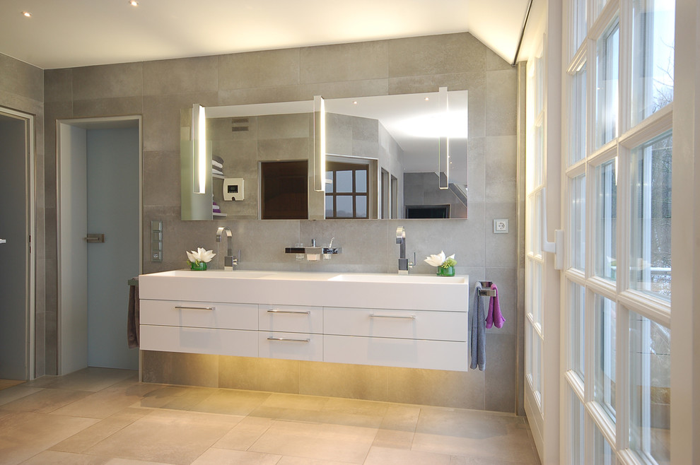 ブレーメンにある広いコンテンポラリースタイルのおしゃれな浴室 (一体型シンク、フラットパネル扉のキャビネット、白いキャビネット、グレーのタイル、石タイル) の写真