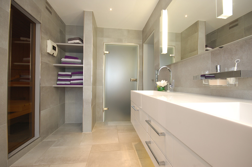 На фото: ванная комната среднего размера в современном стиле с белыми фасадами, серой плиткой, серыми стенами, монолитной раковиной и зеркалом с подсветкой