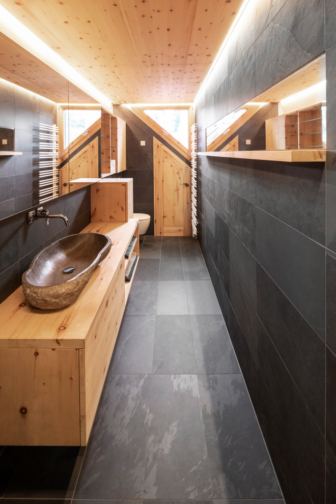 Réalisation d'une petite salle de bain design en bois clair avec un placard à porte plane, une douche à l'italienne, un bidet, un carrelage noir, du carrelage en ardoise, un mur noir, un sol en ardoise, une grande vasque, un plan de toilette en granite, un sol noir, aucune cabine, un plan de toilette marron, des toilettes cachées, meuble simple vasque, meuble-lavabo suspendu et un plafond en bois.
