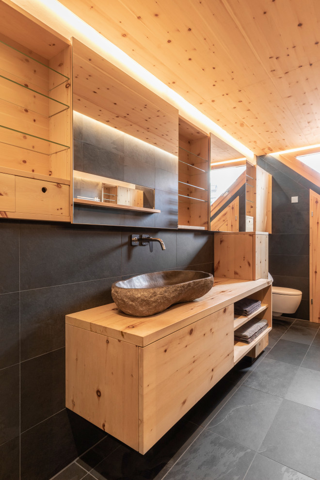 Inspiration för ett litet funkis brun brunt badrum, med släta luckor, skåp i ljust trä, en kantlös dusch, en bidé, svart kakel, skifferkakel, svarta väggar, skiffergolv, ett avlångt handfat, granitbänkskiva, svart golv och med dusch som är öppen