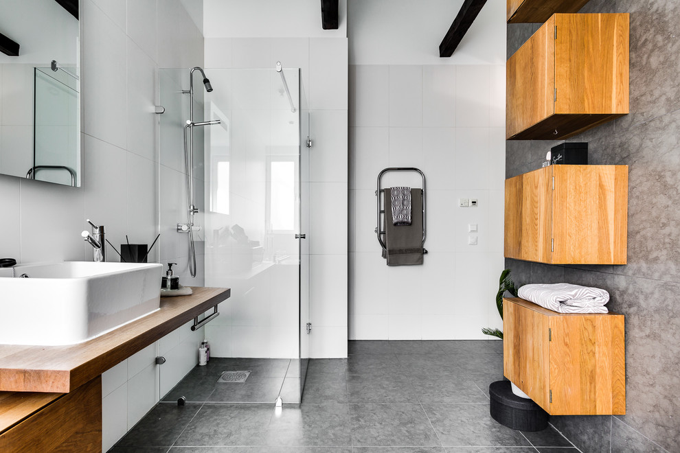 Idéer för ett stort modernt badrum med dusch, med skåp i mellenmörkt trä, en kantlös dusch, en toalettstol med hel cisternkåpa, vit kakel, porslinskakel, vita väggar, ett fristående handfat, träbänkskiva, släta luckor och dusch med gångjärnsdörr