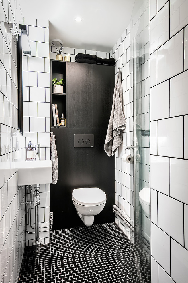 Klassisk inredning av ett mellanstort badrum, med en vägghängd toalettstol, svart och vit kakel, vita väggar, ett väggmonterat handfat, släta luckor, svarta skåp, porslinskakel och mosaikgolv
