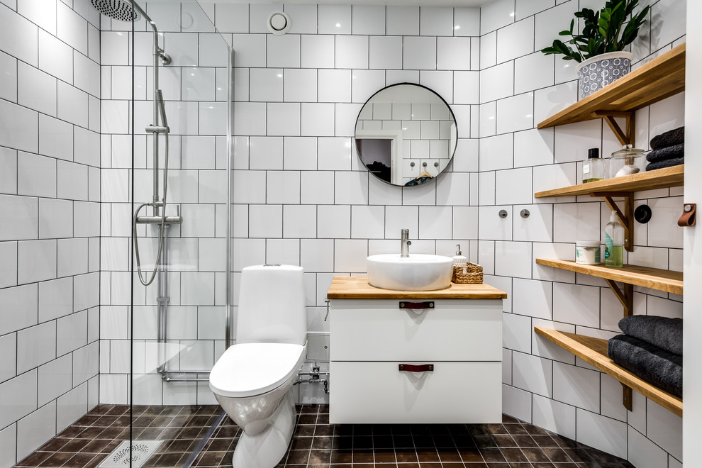 Inspiration for a medium sized scandi shower room bathroom in Stockholm with flat-panel cabinets, white cabinets, a built-in shower, a one-piece toilet, white tiles, white walls, a vessel sink, wooden worktops and brown worktops.