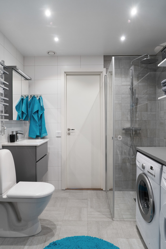 Diseño de cuarto de baño escandinavo de tamaño medio con armarios con paneles lisos, puertas de armario grises, ducha esquinera, sanitario de una pieza, ducha con puerta con bisagras, baldosas y/o azulejos grises, baldosas y/o azulejos blancos, paredes grises, suelo gris y tendedero