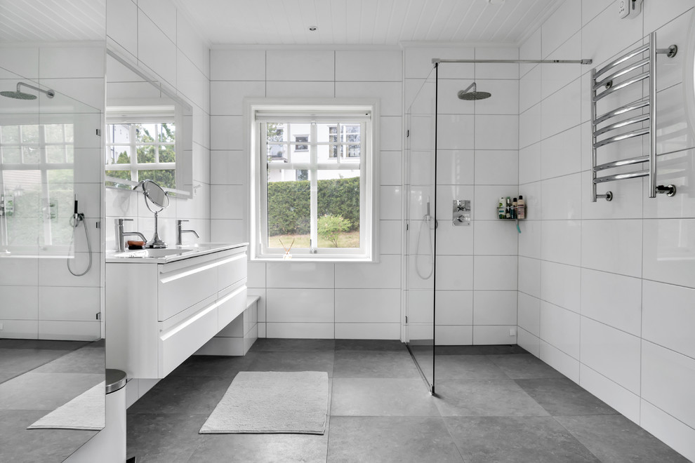 Großes Nordisches Duschbad mit flächenbündigen Schrankfronten, weißen Schränken, weißer Wandfarbe, Unterbauwaschbecken, grauem Boden, Eckdusche, weißen Fliesen und offener Dusche in Stockholm