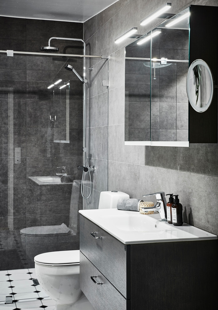 Foto på ett mellanstort funkis badrum med dusch, med släta luckor, skåp i mellenmörkt trä, en toalettstol med hel cisternkåpa, grå kakel, keramikplattor, klinkergolv i keramik, ett avlångt handfat, laminatbänkskiva, en dusch i en alkov, grå väggar, vitt golv och dusch med gångjärnsdörr