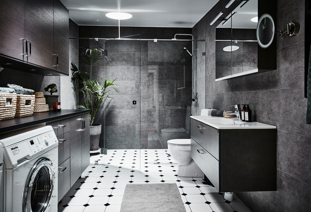 Inredning av ett modernt mellanstort badrum med dusch, med släta luckor, skåp i mellenmörkt trä, en toalettstol med hel cisternkåpa, grå kakel, keramikplattor, klinkergolv i keramik, ett avlångt handfat, laminatbänkskiva, dusch med gångjärnsdörr, en dusch i en alkov, grå väggar och vitt golv