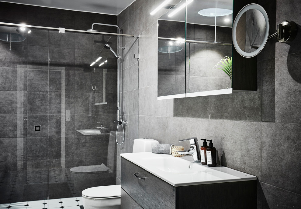 Bild på ett mellanstort funkis badrum med dusch, med släta luckor, skåp i mellenmörkt trä, en toalettstol med hel cisternkåpa, grå kakel, keramikplattor, klinkergolv i keramik, ett avlångt handfat, laminatbänkskiva, en dusch i en alkov, grå väggar, grått golv och dusch med gångjärnsdörr