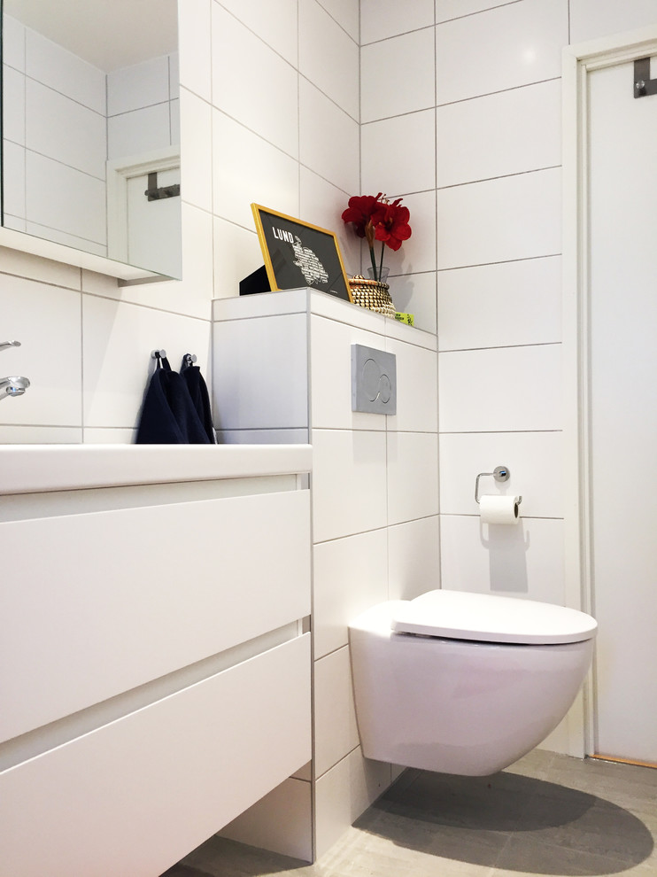 Photo of a medium sized scandi shower room bathroom in Other with flat-panel cabinets, white cabinets, a walk-in shower, a wall mounted toilet, white tiles, cement tiles, white walls, cement flooring, a wall-mounted sink, beige floors and a hinged door.